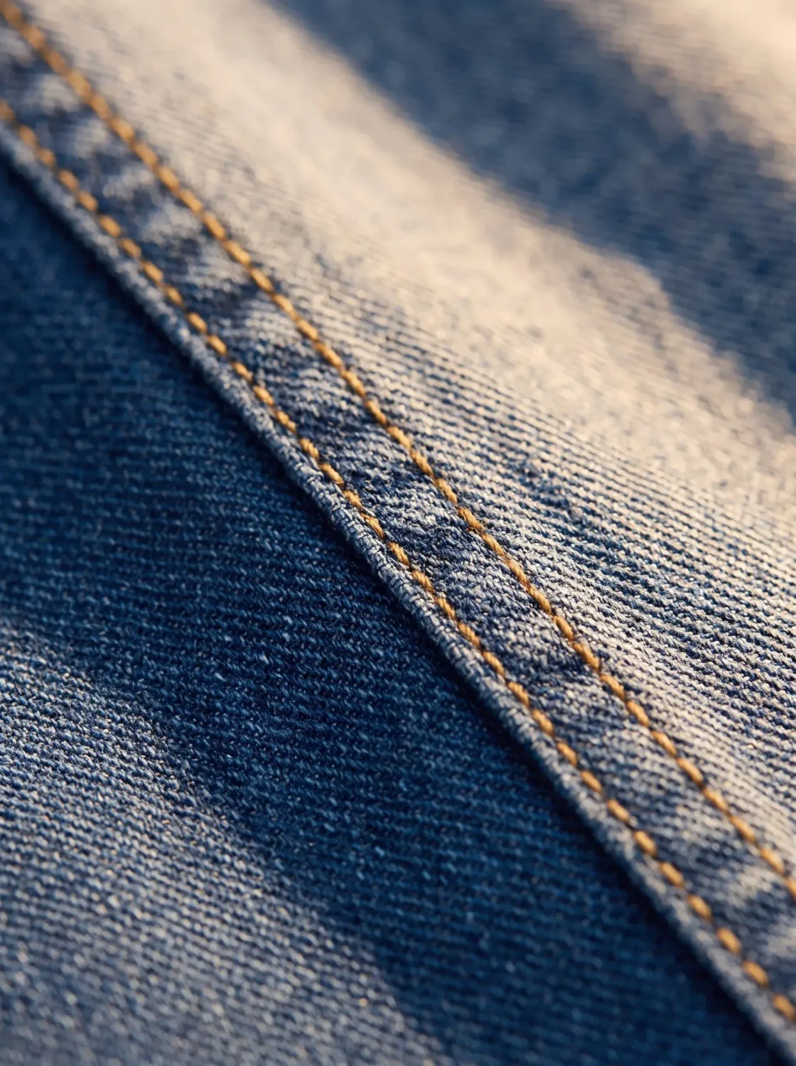 Makroaufnahme einer Denim-Kappnaht mit oranger Steppung auf blauem Gewebe